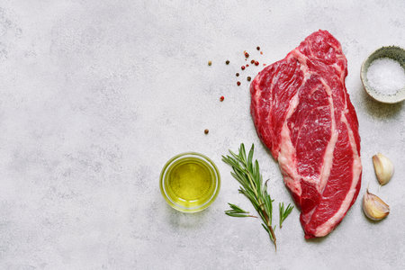 Raw organic marbled beef steak with ingredients for cooking on a light gray slate, stone or concrete background. Top view with copy space.の写真素材