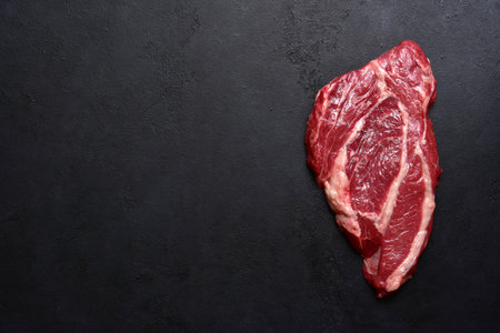 Raw organic marbled beef steak with ingredients for cooking on a black slate, stone or concrete background. Top view with copy space.の写真素材