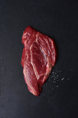 Raw organic marbled beef steak with ingredients for cooking on a black slate, stone or concrete background. Top view with copy space.の写真素材