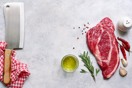 Raw organic marbled beef steak with ingredients for cooking on a light gray slate, stone or concrete background. Top view with copy space.の写真素材