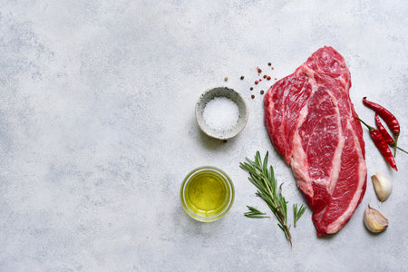 Raw organic marbled beef steak with ingredients for cooking on a light gray slate, stone or concrete background. Top view with copy space.の写真素材