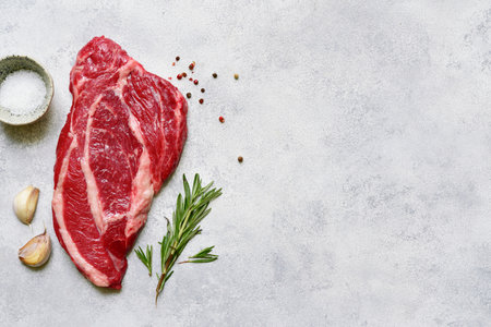 Raw organic marbled beef steak with ingredients for cooking on a light gray slate, stone or concrete background. Top view with copy space.の写真素材