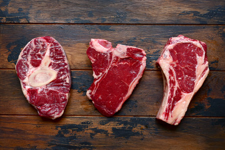Raw organic marbled beef steaks: ossobuko, rib eye (cowboy), T-bone on a rustic wooden background. Top view with copy space.の写真素材