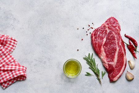 Raw organic marbled beef steak with ingredients for cooking on a light gray slate, stone or concrete background. Top view with copy space.の写真素材