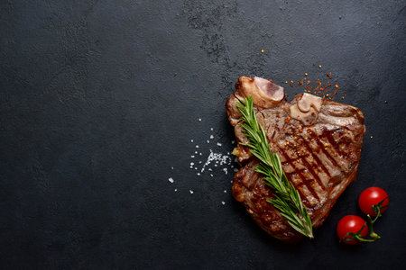 Grilled T-bone beef steak on a dark slate, stone or concrete background. Top view with copy space.の写真素材