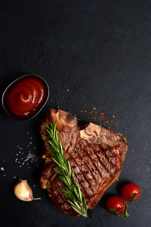 Grilled T-bone beef steak on a dark slate, stone or concrete background. Top view with copy space.の写真素材