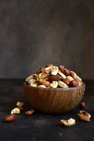 Variety of nuts in a wooden bowl on a dark slate, stone or concrete background.の写真素材