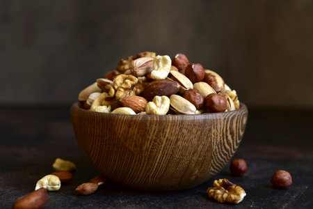 Variety of nuts in a wooden bowl on a dark slate, stone or concrete background.の写真素材