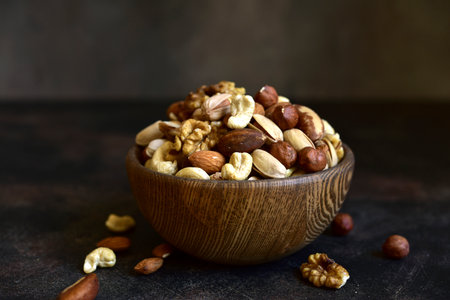 Variety of nuts in a wooden bowl on a dark slate, stone or concrete background.の写真素材