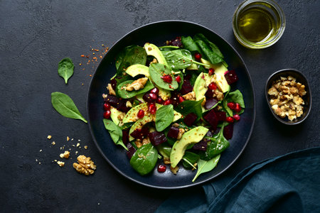 Spinach salad with avocado, beet root, walnuts and pomegranate seeds in a black bowl over dark slate, stone or concrete background. To view with copy space.の写真素材