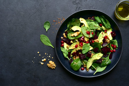 Spinach salad with avocado, beet root, walnuts and pomegranate seeds in a black bowl over dark slate, stone or concrete background. To view with copy space.の写真素材