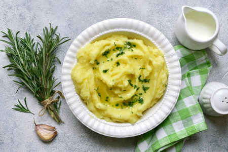 Mashed potato in mediterranean style with rosemary, parmesan cheese, garlic and olive oil on a light slate, stone or concrete background. Top view with copy space.の写真素材