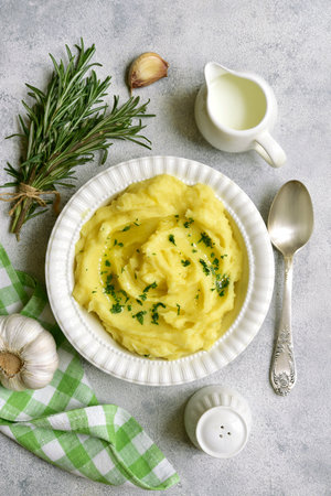 Mashed potato in mediterranean style with rosemary, parmesan cheese, garlic and olive oil on a light slate, stone or concrete background. Top view with copy space.の写真素材