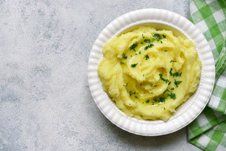 Mashed potato in mediterranean style with rosemary, parmesan cheese, garlic and olive oil on a light slate, stone or concrete background. Top view with copy space.の写真素材