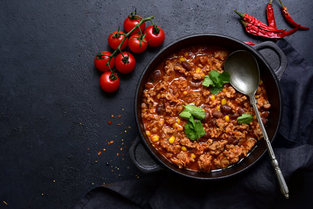 Chili con carne - traditional Mexican minced meat and vegetables stew in tomato sauce in a cast iron pan on a black slate, stone or concrete background. Top view with copy space.の写真素材