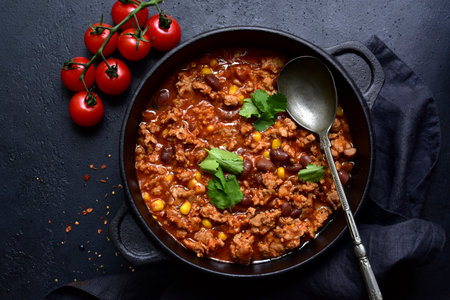 Chili con carne - traditional Mexican minced meat and vegetables stew in tomato sauce in a cast iron pan on a black slate, stone or concrete background. Top view with copy space.の写真素材