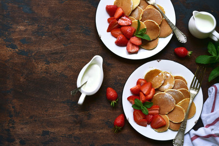 Delicious tiny pancakes with fresh strawberry for a breakfast on a dark rustic wooden background. Top view with copy space.の写真素材