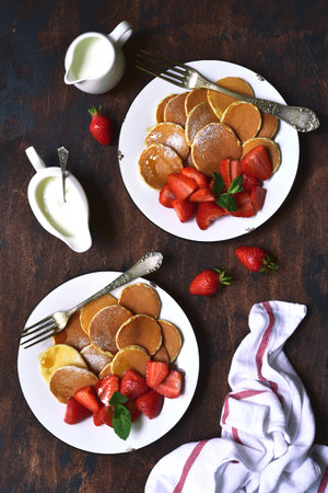 Delicious tiny pancakes with fresh strawberry for a breakfast on a dark rustic wooden background. Top view with copy space.の写真素材