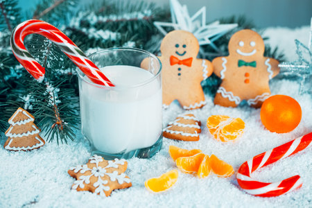 Christmas gingerbread and milk with decorations, snow, christmas tree branches on bokeh blurred lights background. Free spaceの写真素材