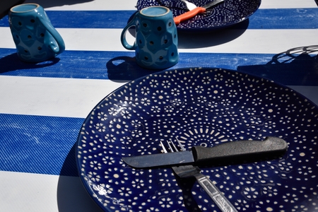 Blue dish with knife and fork on right on white and blue table with blue cupの写真素材