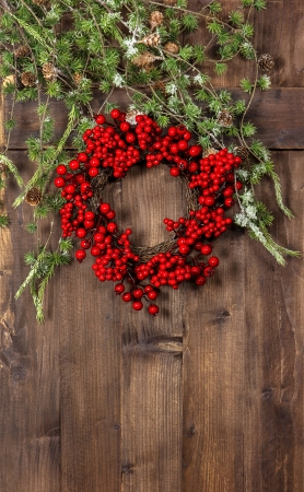 green christmas tree branches and wreath from red berries over rustic wooden background. festive home decorationの写真素材