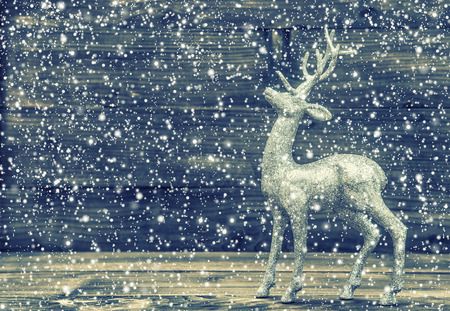 Christmas deer. Vintage style decoration on wooden background. Retro style toned picture with falling snow effectの写真素材
