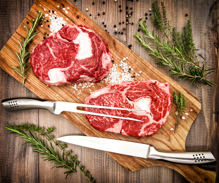 Raw fresh beef meat with herbs and spices on wooden background. Retro style toned photoの写真素材