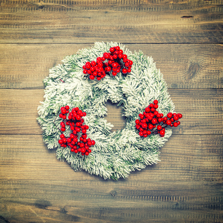 Christmas wreath with red berries over wooden background. Festive decoration. Vintage style toned pictureの写真素材