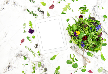 Food background tablet PC. Green salad with herbs and flowers. Healthy organic nutrition. Digital recipe bookの写真素材