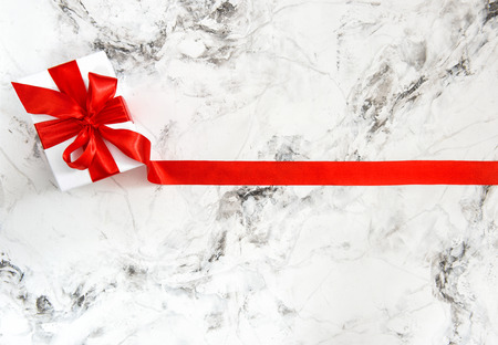 Gift box with red ribbon bow on bright marble backgroundの写真素材