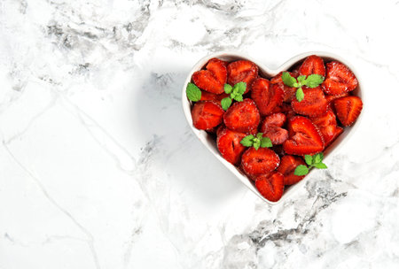 Strawberry fruits heart with green mint leaves on white marble background. Food. Berriesの写真素材