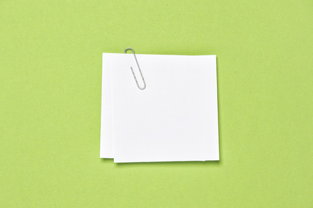 White empty note paper sheet with paperclip on green backgroundの写真素材