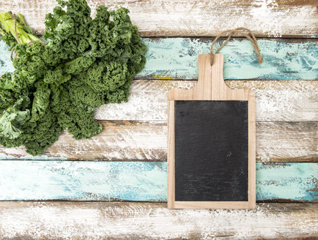 Kale cabbage and kitchen blackboard. Green vegetable leaves on rustic wooden backgroundの写真素材