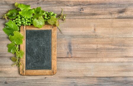 Chalkboard with grapes and green vine leaves decoration on wooden backgroundの写真素材