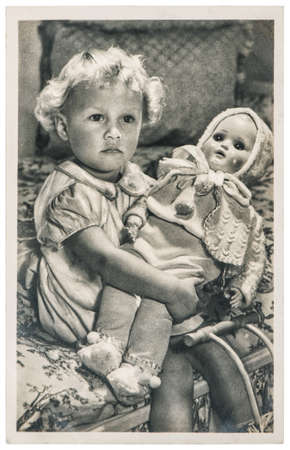 Little girl with a big baby doll. Vintage picture with original film grain and blurのeditorial素材