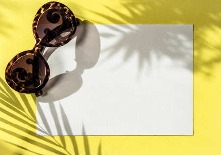 Blank paper mockup. Shadow of palm leaves on yellow background. Summer flat lay sunglassesの写真素材