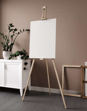 Blank canvas on wooden easel with chest of drawers, plant
And beige wall. 3d renderingの写真素材