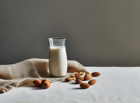 Organic almond milk in glass bottle near ceramic bowl with raw almonds on stone table in the kitchen ready for cookingの写真素材
