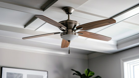 A white ceiling fan with five blades and three lights hangs from a white ceiling. The fan has gold accents around the motor and light fixtures. The lights are covered in white shades.の素材