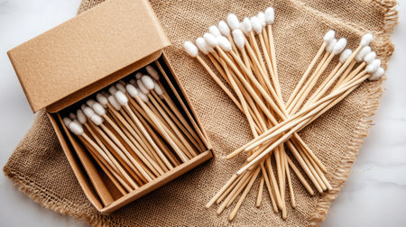 Wooden cotton swabs are neatly arranged in a kraft paper box, resting on jute fabric, illuminated by soft lighting that enhances the natural colors and fine details.の素材