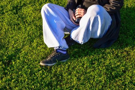 Young girl sitting on the green grass of the football field, in casual sports clothes and holding a cameraの写真素材