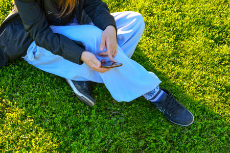 Young girl sitting on the green grass in the hands of smartphoneの写真素材