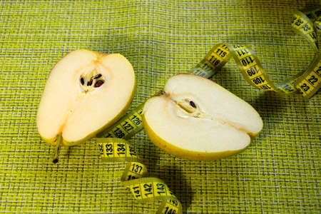 A ripe yellow pear cut in half lies on a napkin next to a centimeter-long ribbon. Useful nutrition for weight loss. Diet fruits.の写真素材