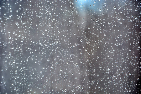 Raindrops on the transparent window pane. Rainy weather outside the window. Abstract background with...