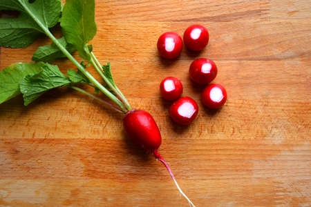 Freshly picked radishes lie on the cutting Board. A bunch of radishes on a wooden background. Growing vegetables. The view from the top. Slices of red radish with leaves.の写真素材