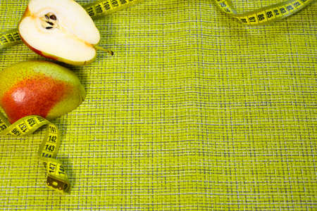 Cut pear and measuring tape. Products for proper nutrition, weight loss and diet. Horizontal photo with a green background.の写真素材