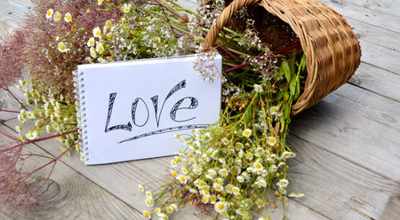Postcard Love. Basket with wild flowers and an inscription on the notebook Love. The word is written...