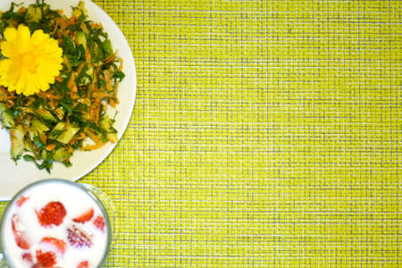 Green background with food plates and space for text. Salad with nasturtium flower and a glass of milk and strawberries on a napkin.の写真素材