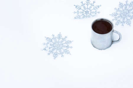 Christmas background with snowflakes and a mug of hot coffee in the snow. Snowflakes around an old metal mug with a coffee drink on the street.の写真素材