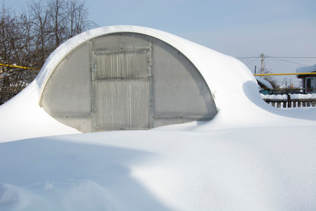 Greenhouse in the snow. High snowdrifts in the winter dacha. Snowy vegetable garden in the winter.の写真素材